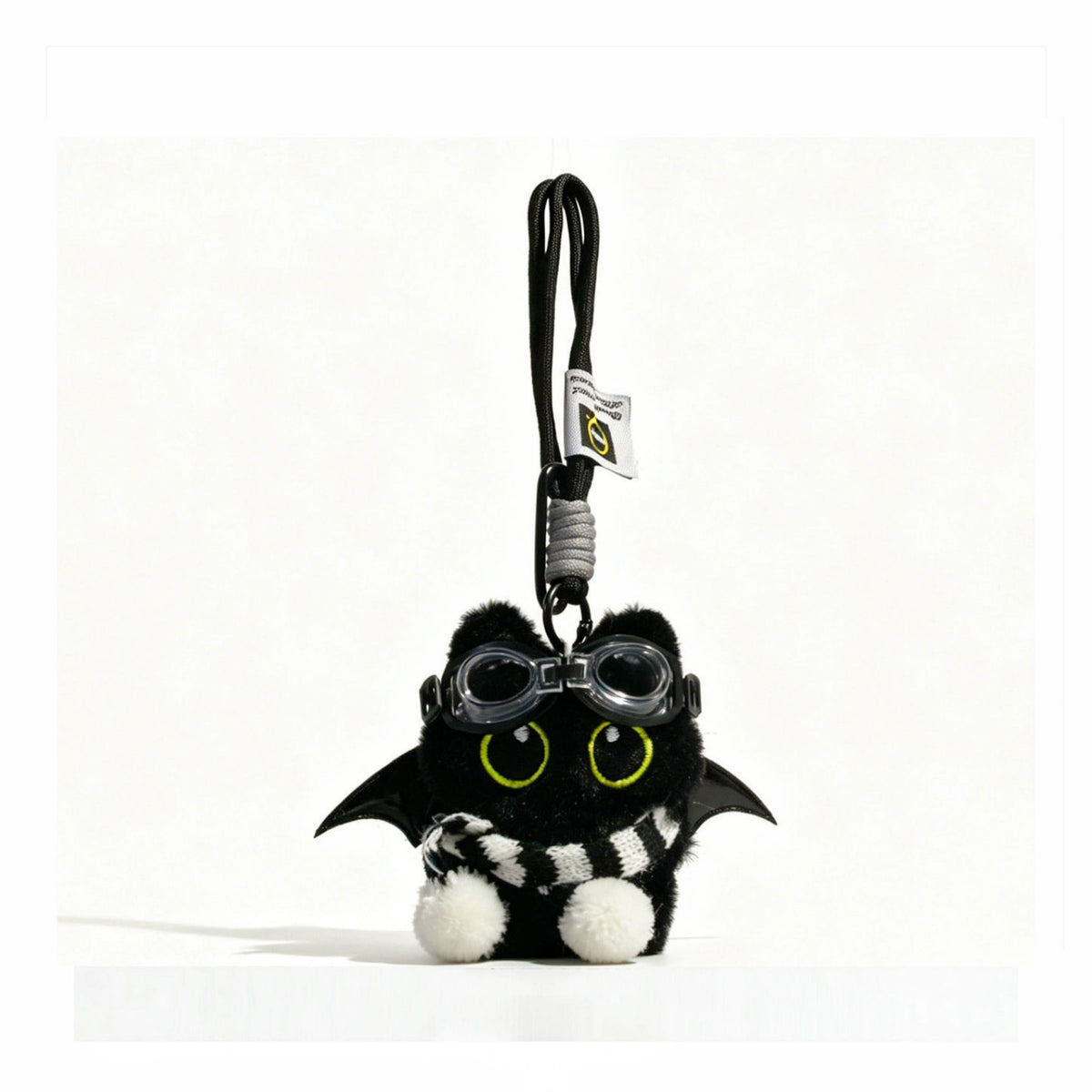 Close-up of a black plush bat-winged Yoyo keychain wearing goggles and a black-and-white striped scarf