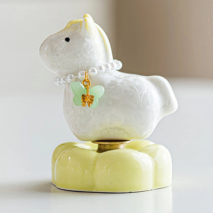 Close-up of a ceramic Heavenly Steed unicorn figurine in pale yellow with a pearl necklace and butterfly charm