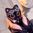 Black plush Yoyo keychain wearing goggles and a studded collar, held outdoors