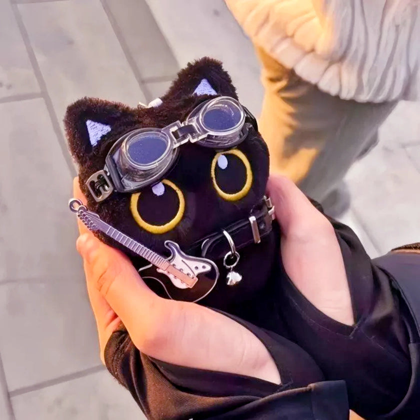 Black plush Yoyo keychain wearing goggles and a studded collar, held outdoors
