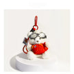 White plush Spirit Bear keychain wearing goggles, holding a red fish charm, on a white pedestal