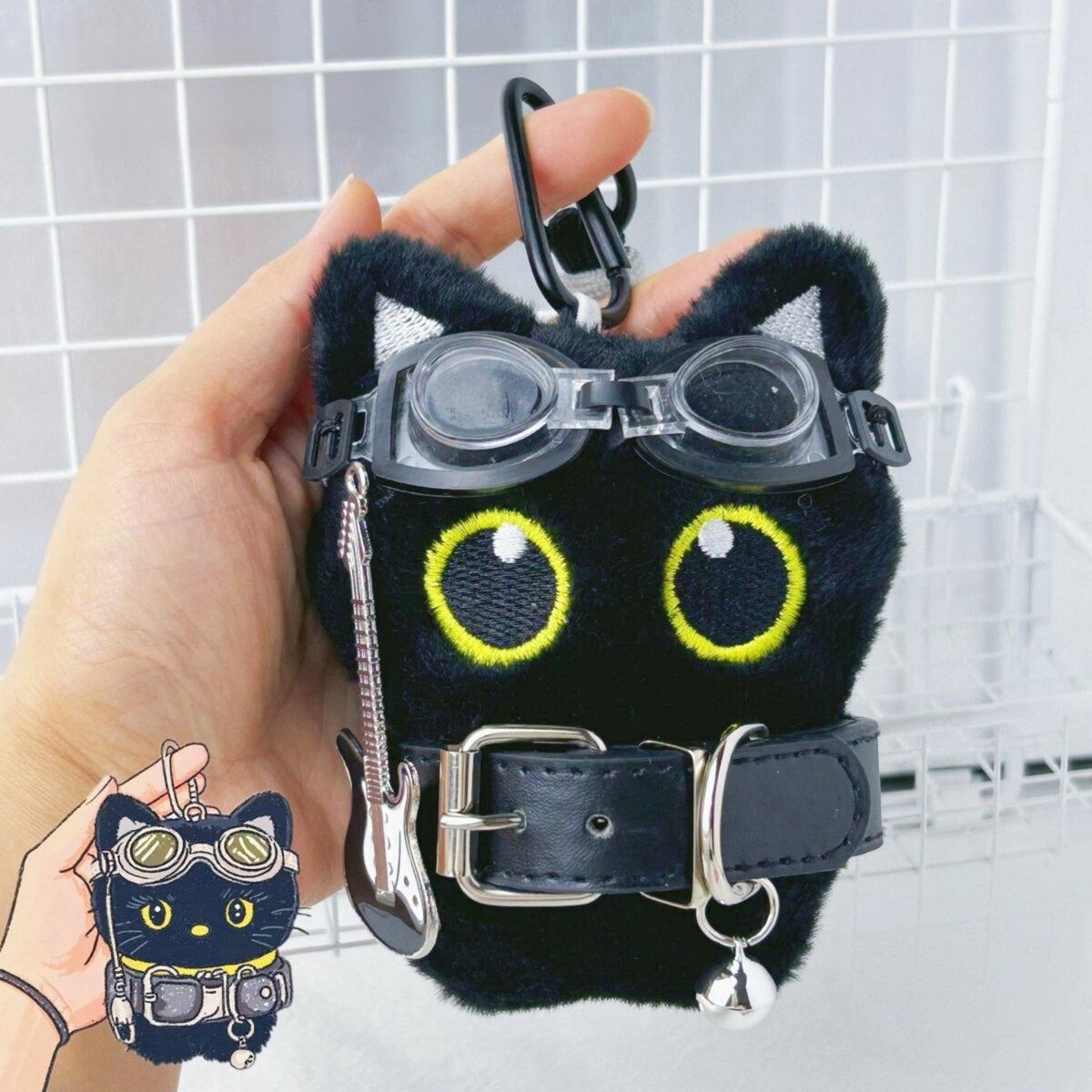 Hand holding a black plush Yoyo keychain wearing goggles and a studded collar with a guitar charm