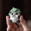 Hand holding a ceramic Spirit Panda figurine with a green leaf hat to show its size