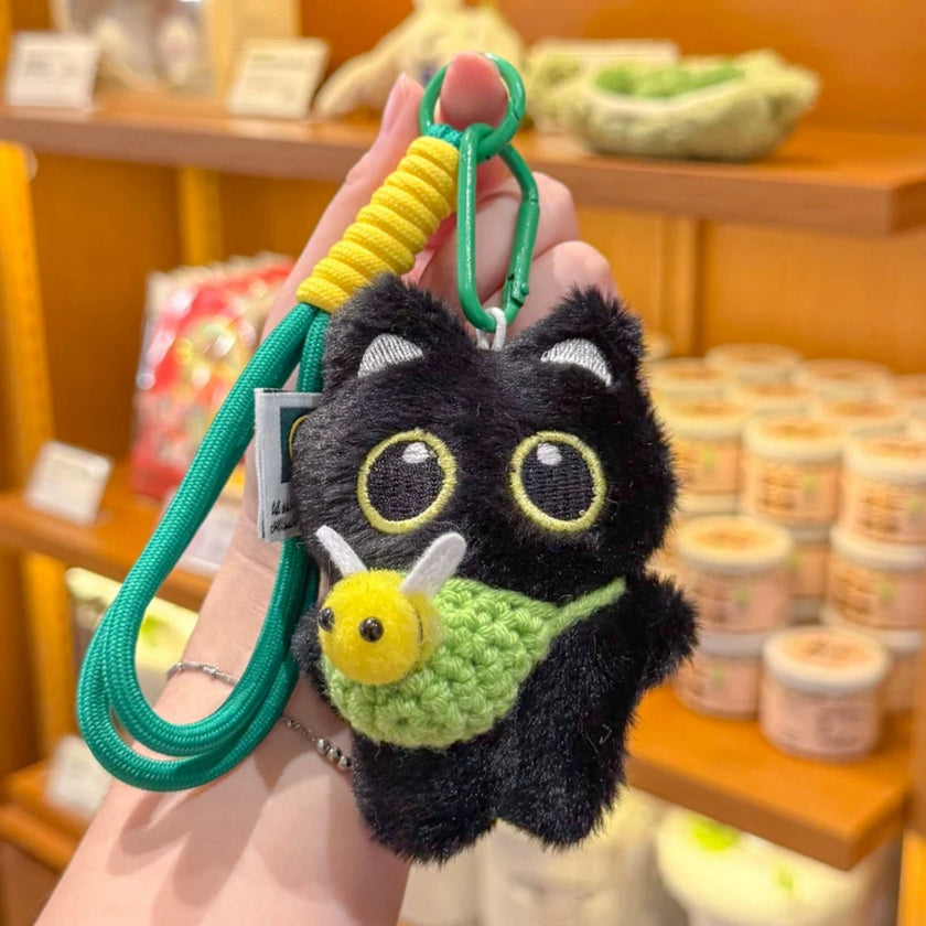 Hand holding a black plush Yoyo keychain with a green crocheted bee pouch in a shop setting