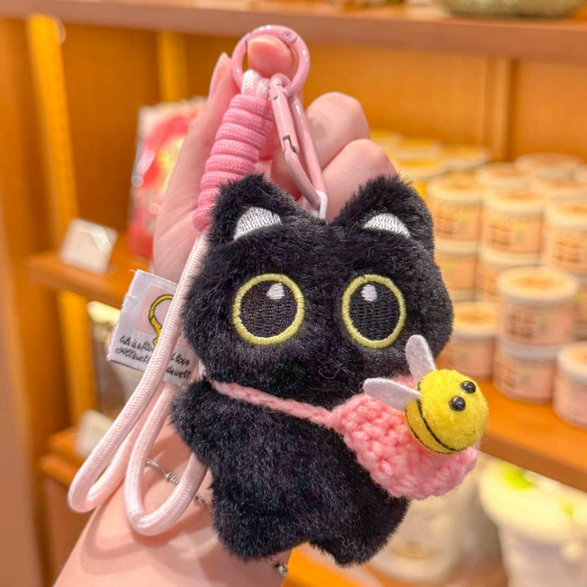Hand holding a black plush Yoyo keychain with a pink crocheted bee pouch in a shop setting