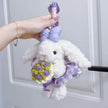 White plush Spirit Rabbit keychain wearing a lilac bow and plaid skirt, held in hand with a crocheted bouquet