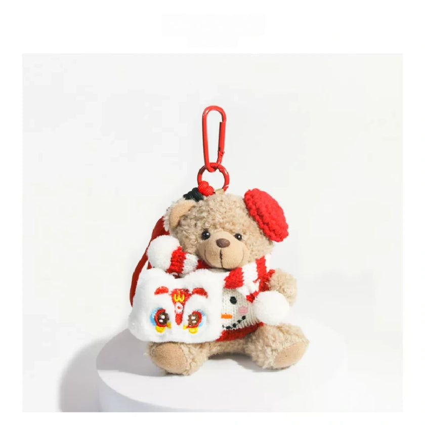 Tan plush Spirit Bear keychain wearing a red beret and scarf, holding a Lucky Lion charm