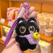 Hand holding a black plush Yoyo keychain with a lavender crocheted bee pouch in a shop setting
