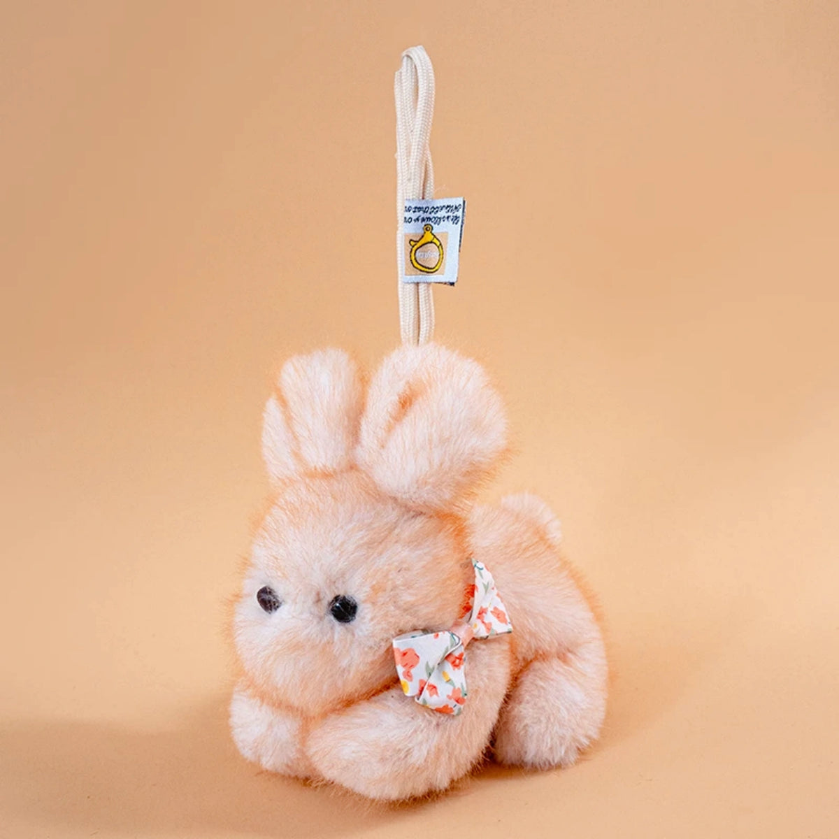Tan plush Spirit Rabbit keychain viewed from behind, wearing an orange floral-print bow