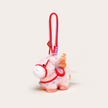 Close-up of a white plush Heavenly Steed horse keychain with an orange bridle and red-topped charm