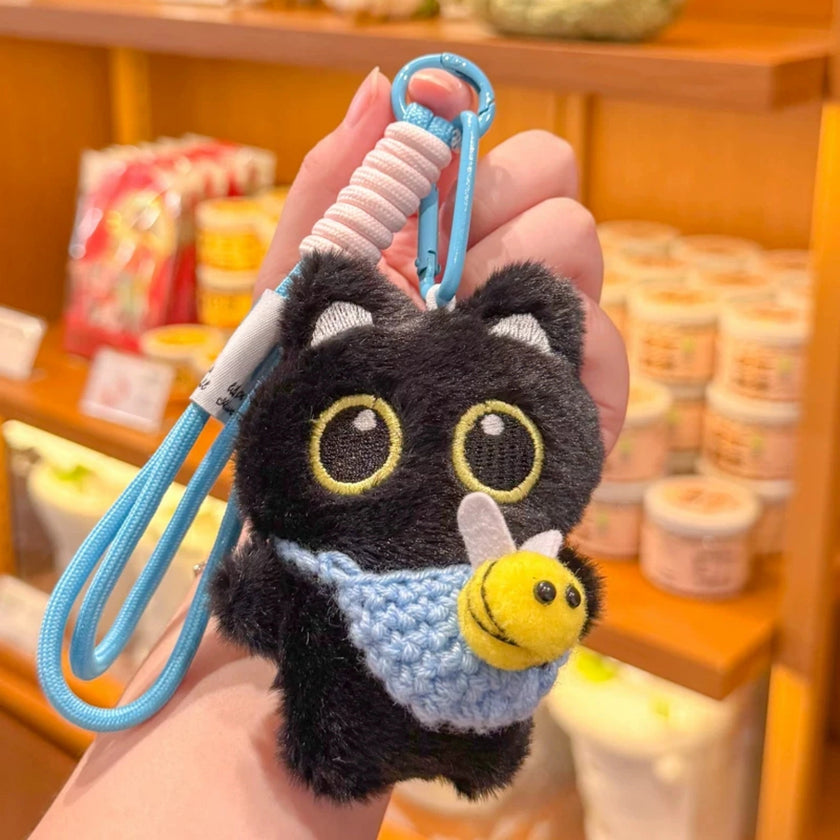Hand holding a black plush Yoyo keychain with a light blue crocheted bee pouch in a shop setting