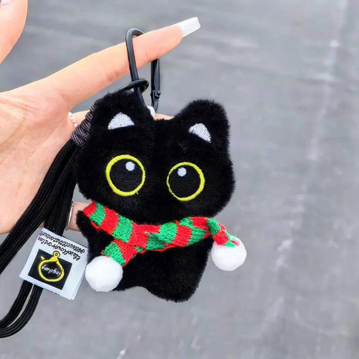 Hand holding a black plush Yoyo keychain wearing a red-and-green striped knitted scarf