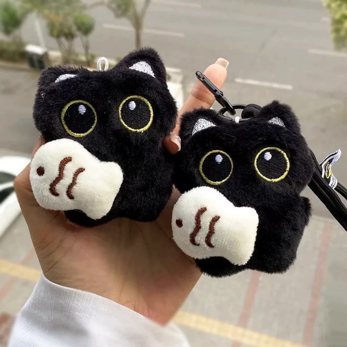 Two black plush Yoyo keychains each holding a cream Cozy Fish charm, held outdoors