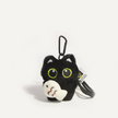 Close-up of a black plush Yoyo keychain holding the cream Cozy Fish charm with wave embroidery