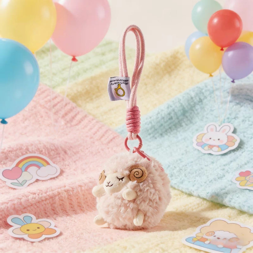 Pink plush Spirit Sheep keychain on a pastel blanket, alternate angle