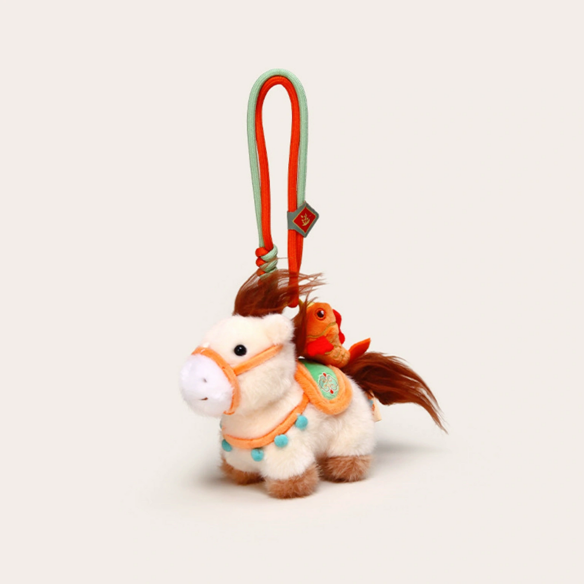 Close-up of a cream plush Heavenly Steed horse keychain with an orange bridle and bird charm