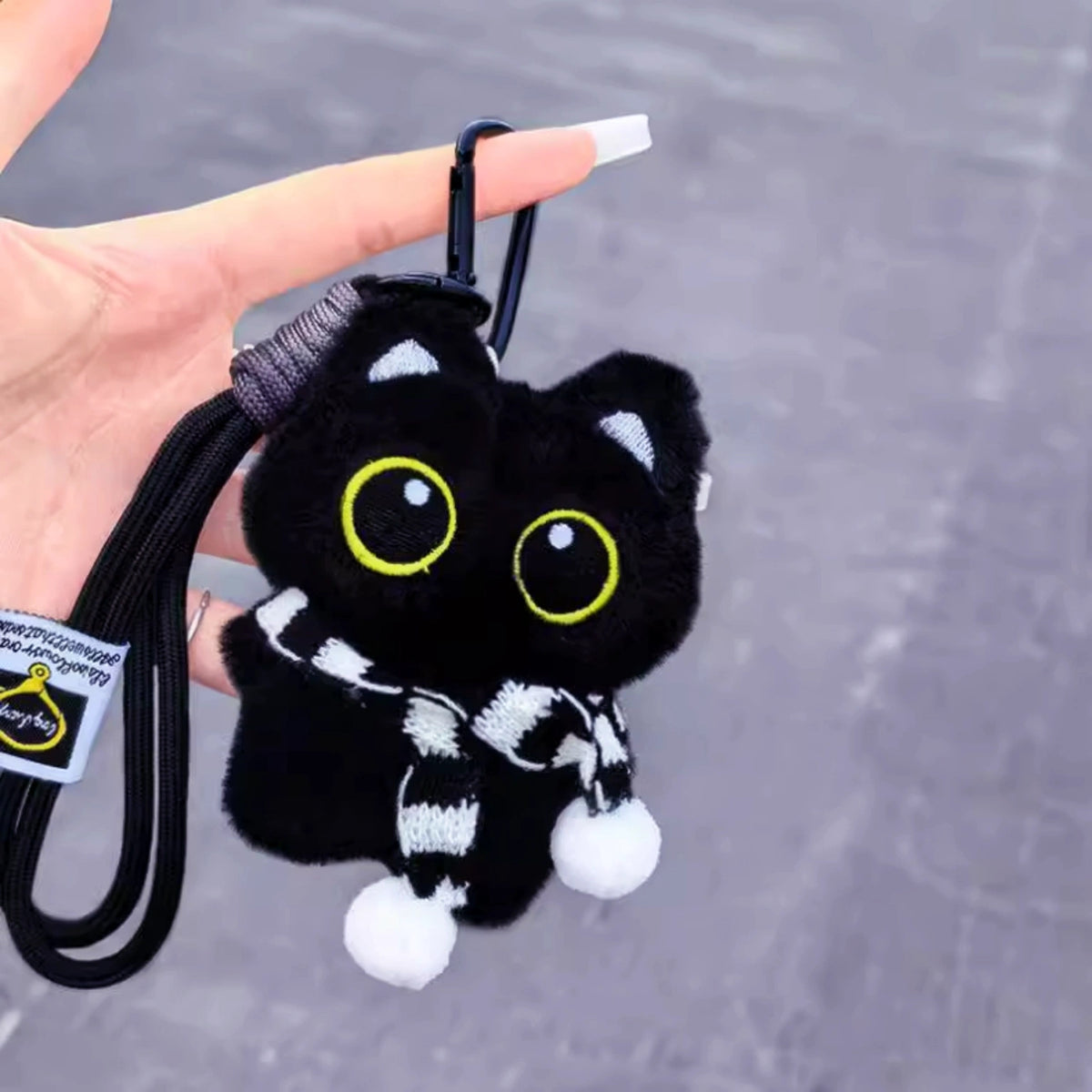 Hand holding a black plush Yoyo keychain wearing a black-and-white striped knitted scarf