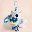 Westie plush keychain wearing a blue sweater, holding a crocheted blue rose bouquet, lifestyle close-up