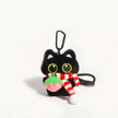 Close-up of a black plush Yoyo keychain wearing a striped scarf and holding a pink strawberry charm