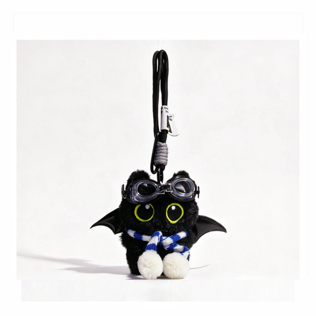 Close-up of a black plush bat-winged Yoyo keychain wearing goggles and a blue-and-white striped scarf