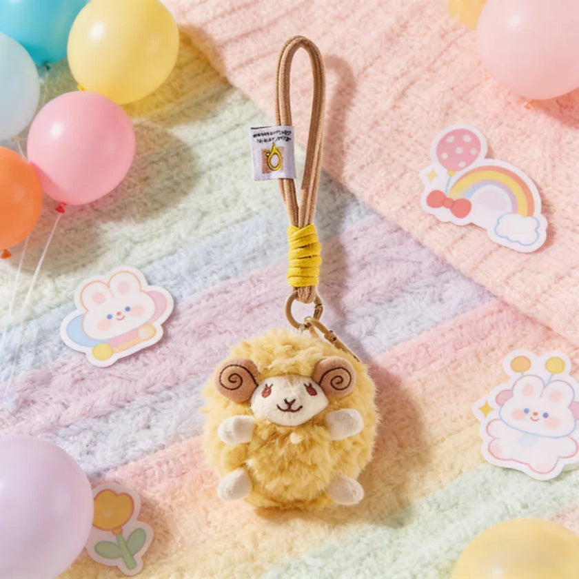 Yellow plush Spirit Sheep keychain resting on a pastel blanket with balloons and stickers