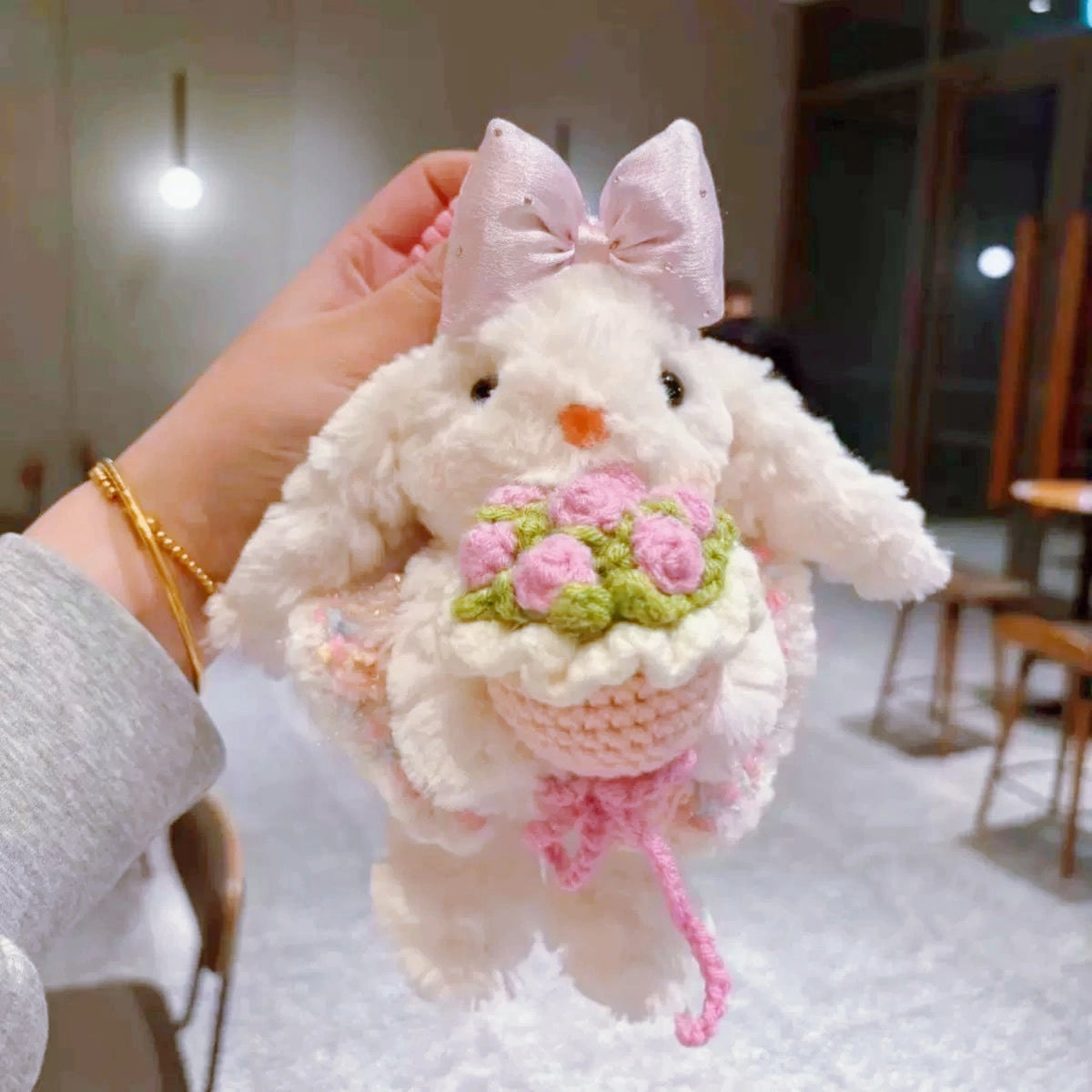 White plush Spirit Rabbit keychain wearing a pink satin bow, held in hand with a crocheted pink flower bouquet