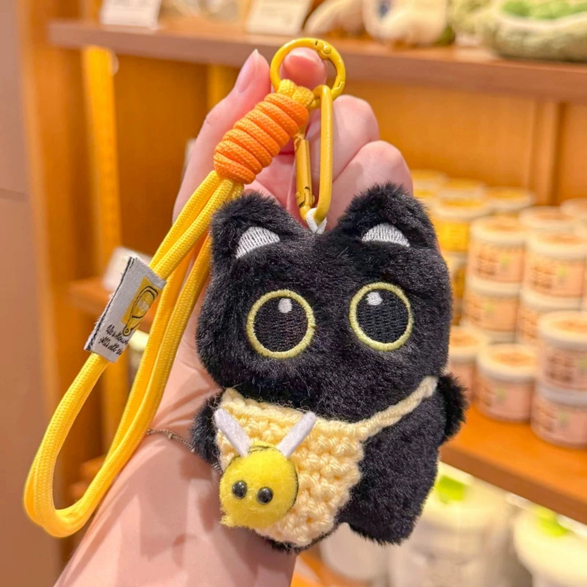 Hand holding a black plush Yoyo keychain with a yellow crocheted bee pouch in a shop setting