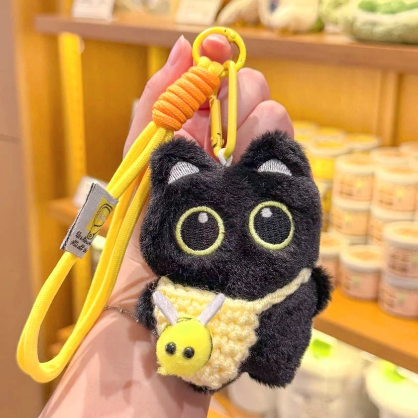 Hand holding a black plush Yoyo keychain with a yellow crocheted bee pouch, alternate angle