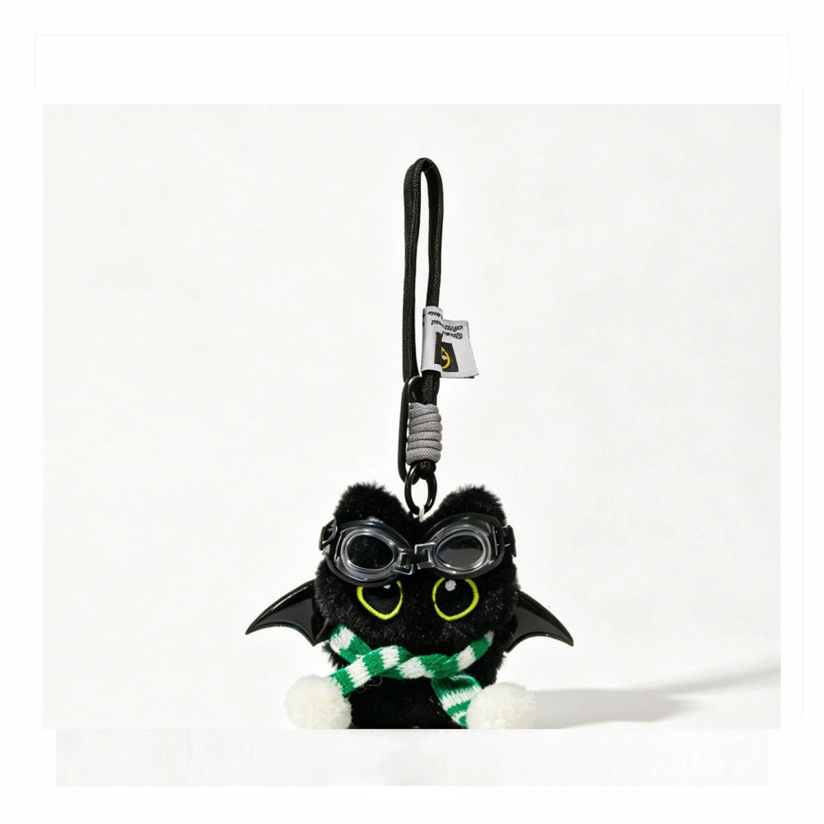 Close-up of a black plush bat-winged Yoyo keychain wearing goggles and a green-and-white striped scarf