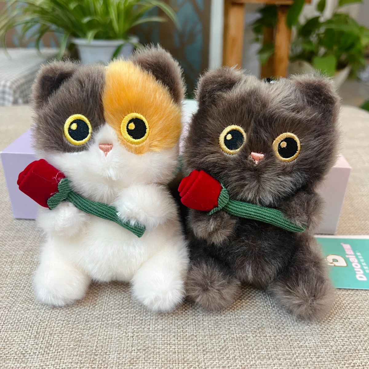 Calico and brown plush Spirit Cat keychains together, each holding a red rose