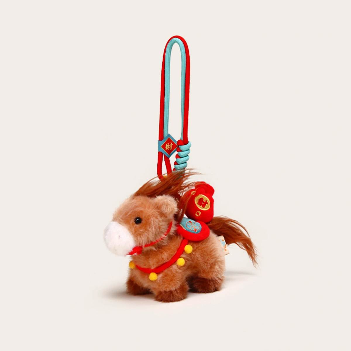 Close-up of a brown plush Heavenly Steed horse keychain with a red saddle and prosperity charm