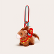 Close-up of a brown plush Heavenly Steed horse keychain with a red saddle and prosperity charm