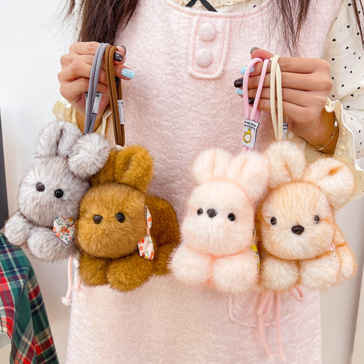 Person holding four plush Spirit Rabbit keychains in gray, brown, pink, and cream, each with a floral bow