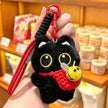 Hand holding a black plush Yoyo keychain with a red crocheted bee pouch in a shop setting
