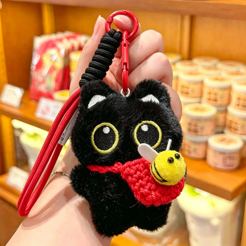 Hand holding a black plush Yoyo keychain with a red crocheted bee pouch in a shop setting